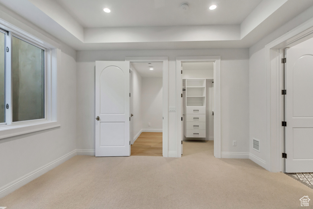 Unfurnished bedroom featuring a closet, a spacious closet, a raised ceiling, and light carpet