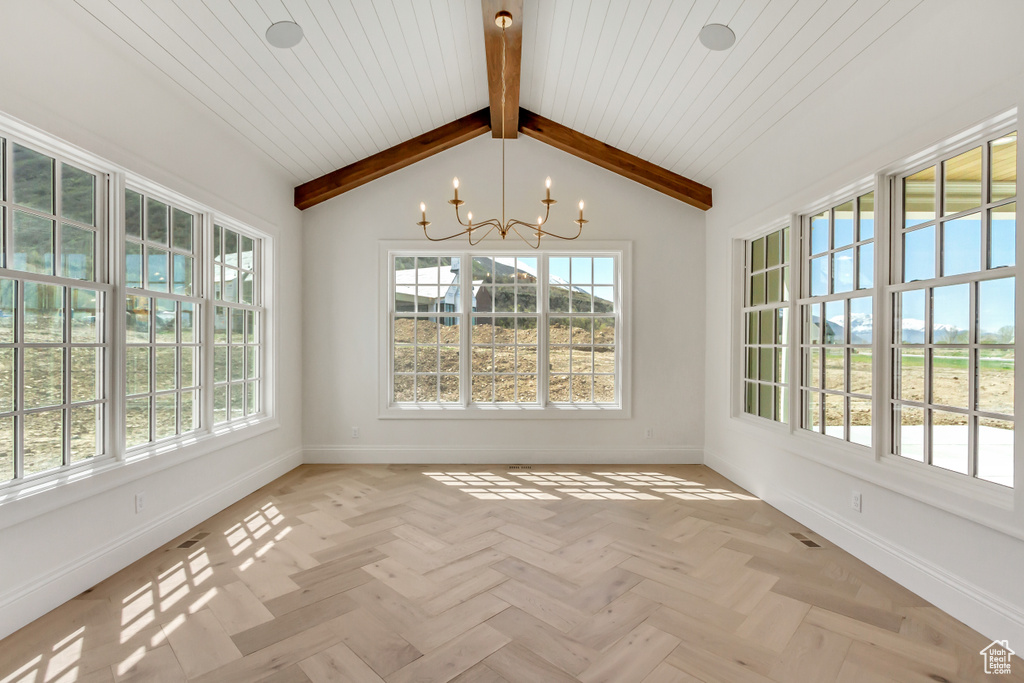 Interior space with a healthy amount of sunlight, lofted ceiling with beams, a notable chandelier, and light parquet flooring