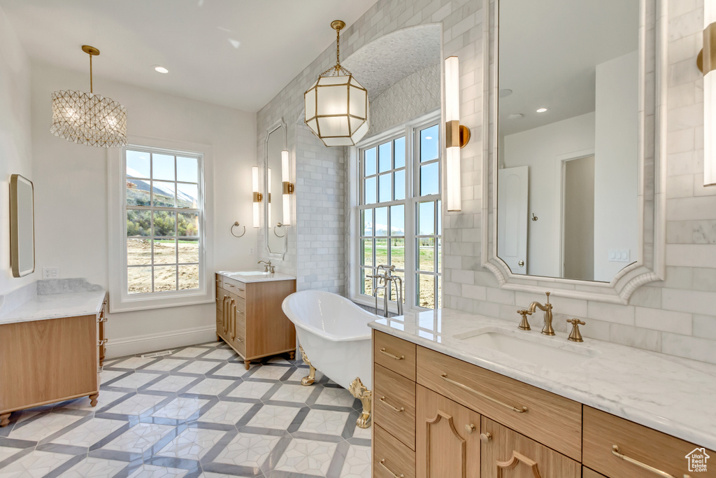 Bathroom featuring dual bowl vanity, a bath to relax in, tile flooring, a notable chandelier, and tasteful backsplash