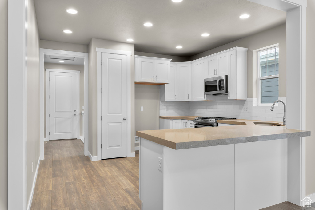 Kitchen featuring white cabinets, kitchen peninsula, sink, tasteful backsplash, and light hardwood / wood-style floors