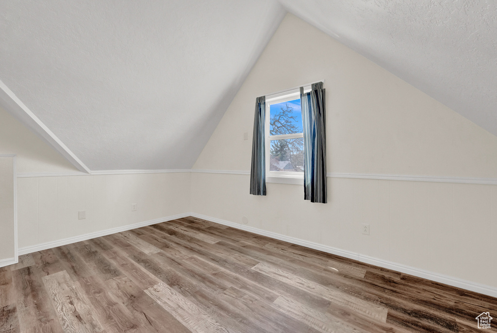 Additional living space featuring a textured ceiling, hardwood / wood-style floors, and lofted ceiling