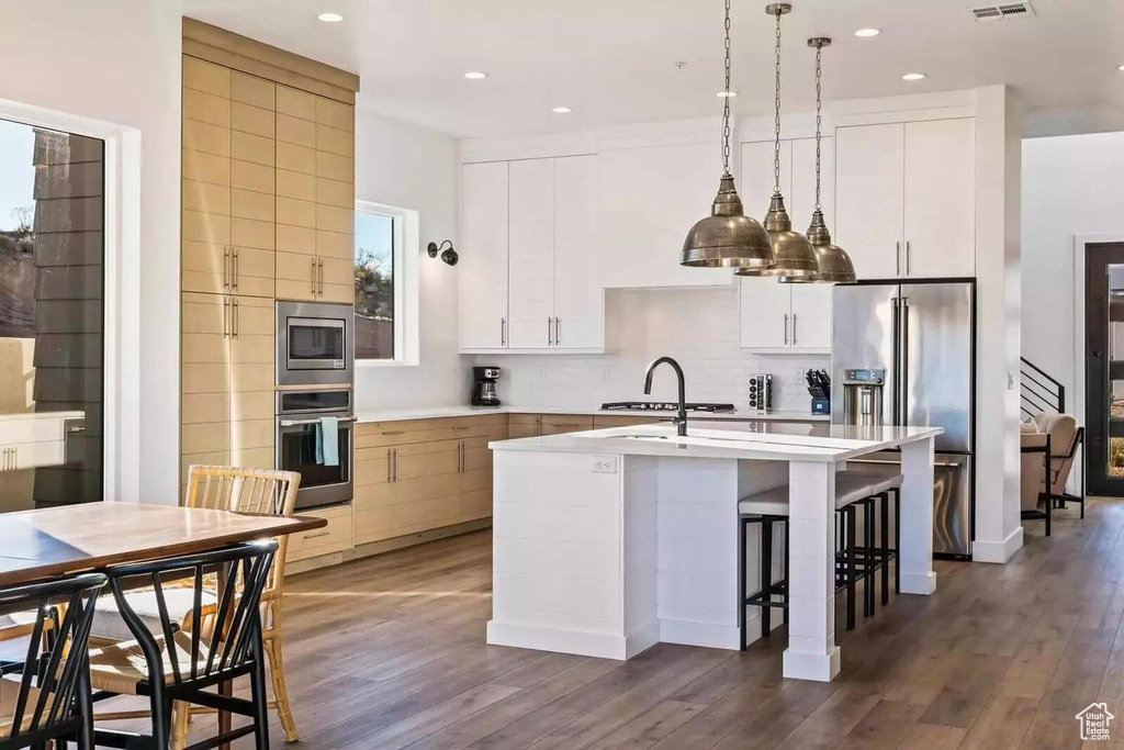 Kitchen featuring appliances with stainless steel finishes, dark hardwood / wood-style floors, white cabinets, and a kitchen island with sink