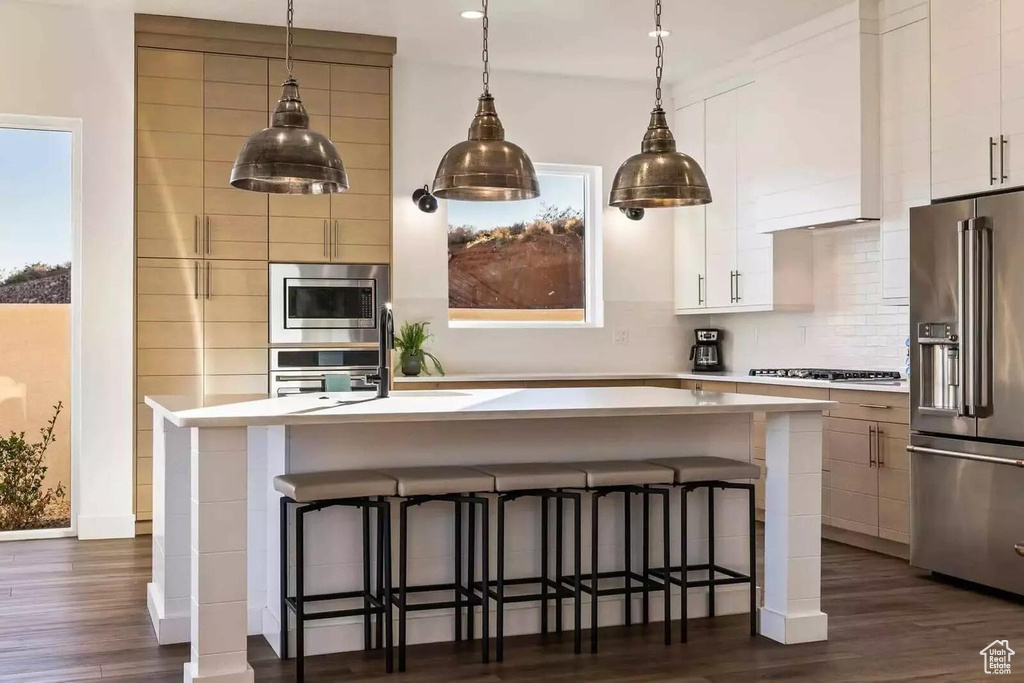 Kitchen featuring a center island with sink, white cabinetry, stainless steel appliances, and dark wood-type flooring