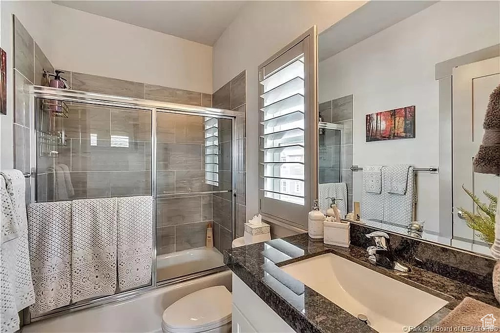 Full bathroom with shower / bath combination with glass door, vanity, and toilet