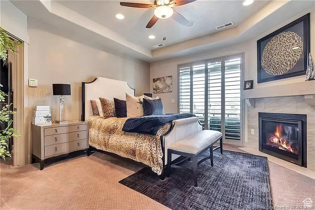 Bedroom featuring ceiling fan, a tray ceiling, a fireplace, and carpet floors