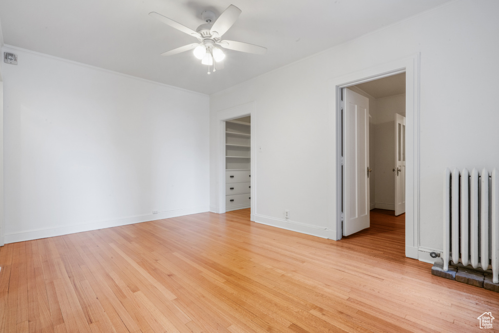 Unfurnished room with light hardwood / wood-style flooring, ceiling fan, and radiator heating unit