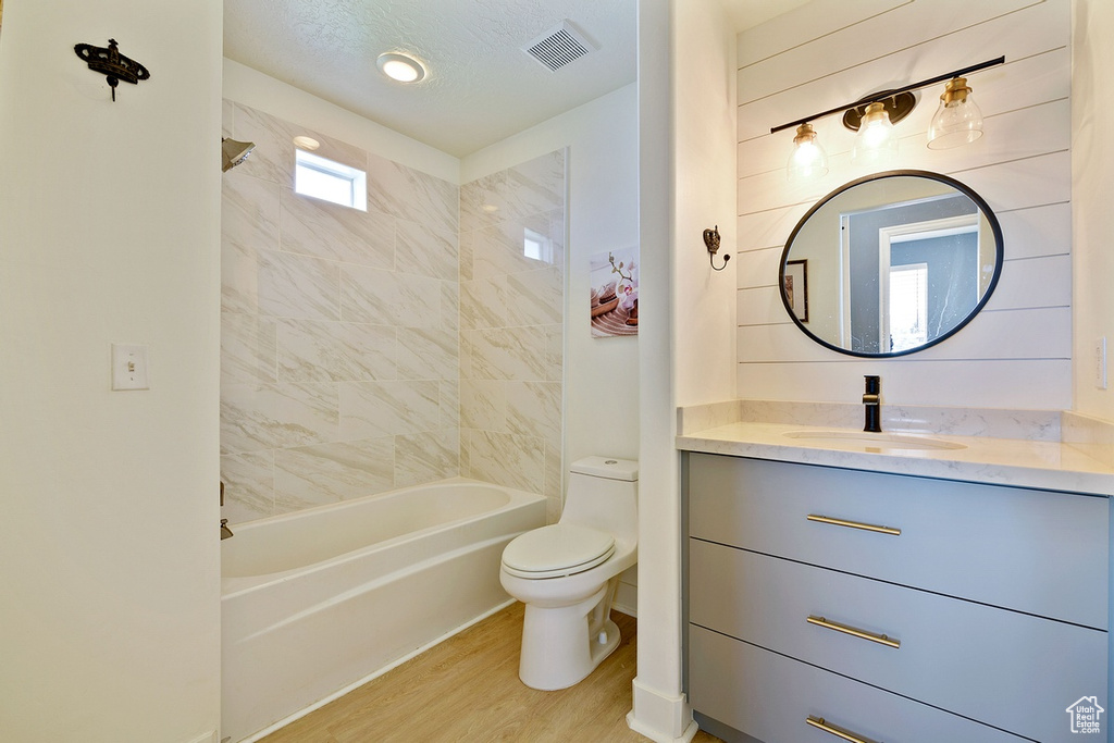 Full bathroom featuring toilet, tiled shower / bath, a textured ceiling, vanity, and hardwood / wood-style floors