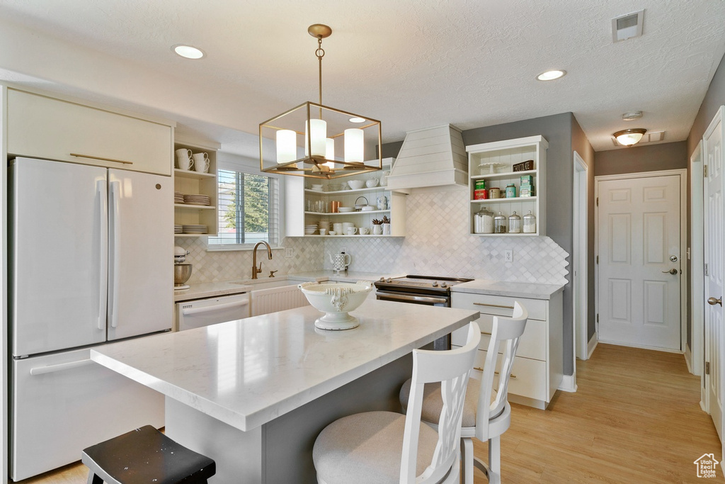Kitchen with a breakfast bar area, white appliances, tasteful backsplash, and custom range hood