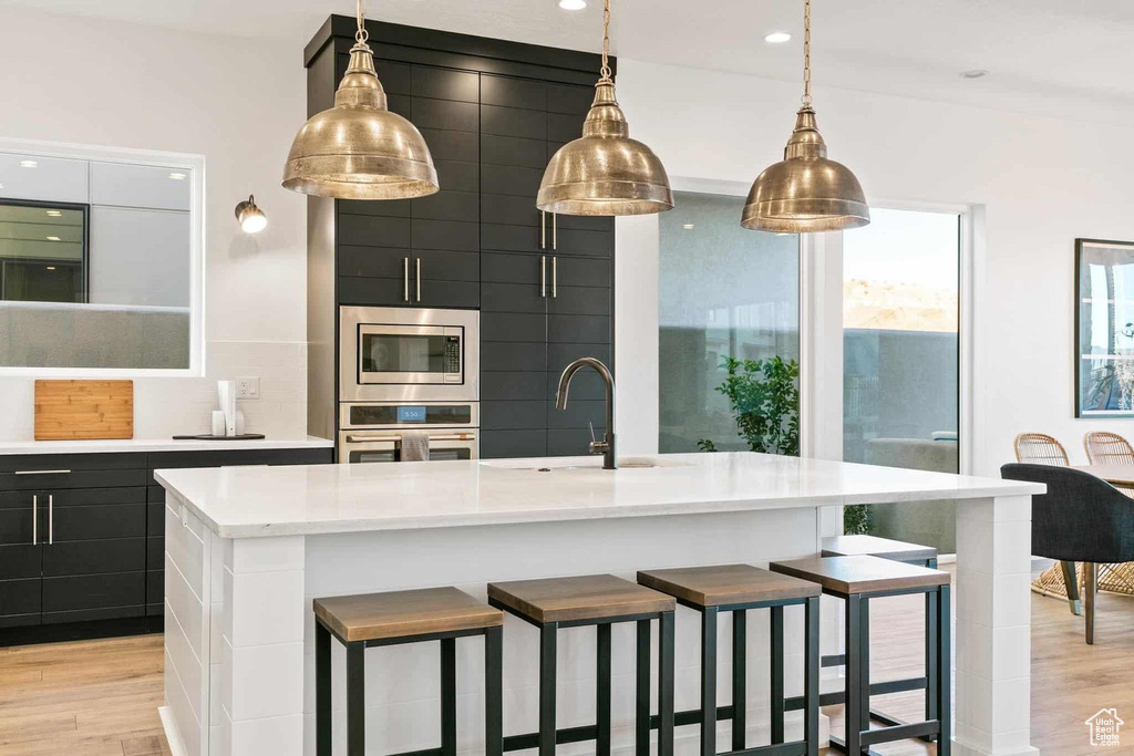 Kitchen with appliances with stainless steel finishes, pendant lighting, a center island with sink, and light hardwood / wood-style floors