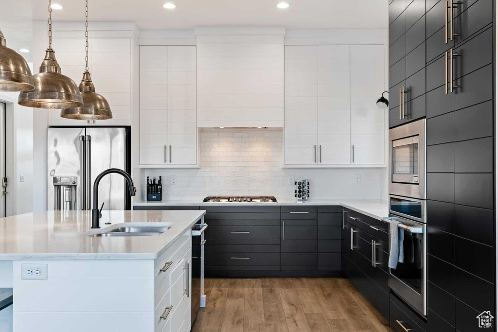 Kitchen with pendant lighting, white cabinets, stainless steel appliances, sink, and light hardwood / wood-style floors