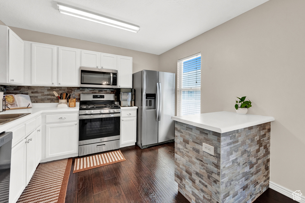 Kitchen with appliances with stainless steel finishes, tasteful backsplash, dark wood-type flooring, white cabinets, and sink