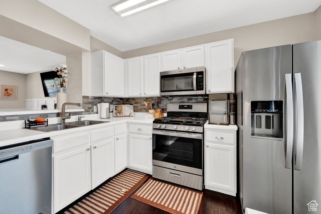 Kitchen featuring appliances with stainless steel finishes, dark hardwood / wood-style floors, tasteful backsplash, white cabinets, and sink