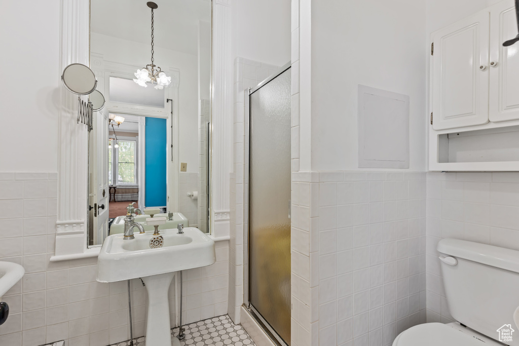 Bathroom with tile flooring, tile walls, a notable chandelier, an enclosed shower, and toilet