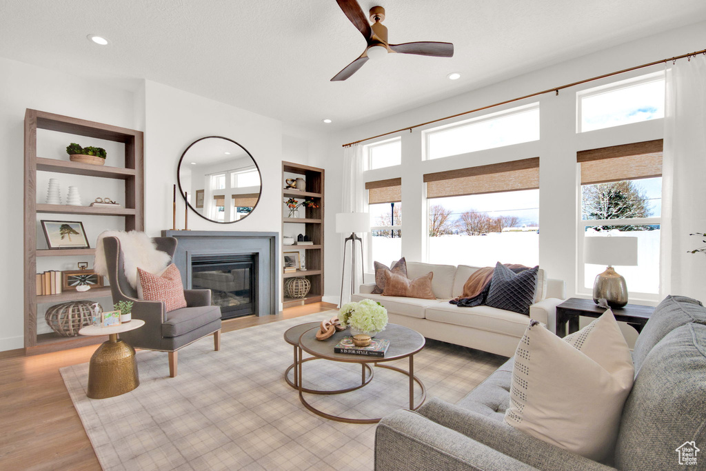 Living room with built in shelves, plenty of natural light, ceiling fan, and light wood-type flooring