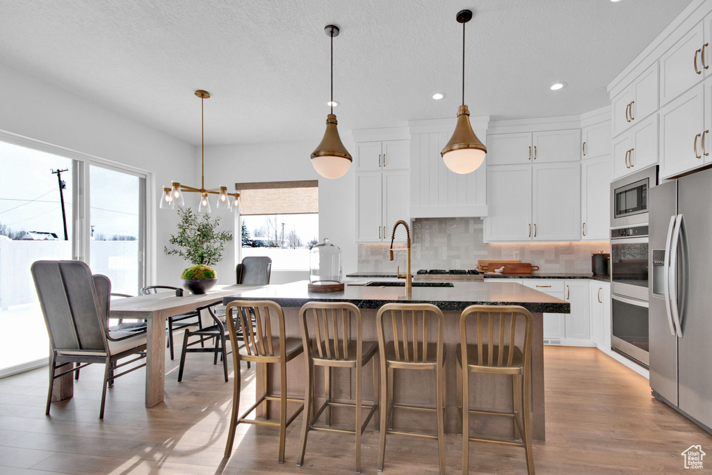 Kitchen with pendant lighting, a kitchen island with sink, light wood-type flooring, backsplash, and stainless steel appliances