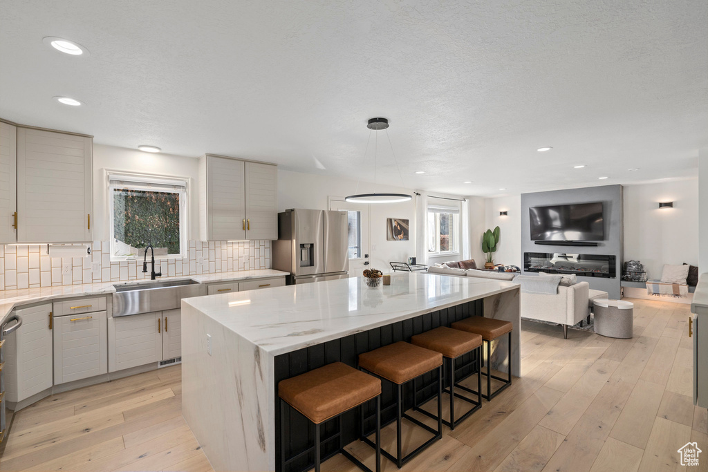 Kitchen with a center island, light hardwood / wood-style flooring, backsplash, sink, and stainless steel fridge