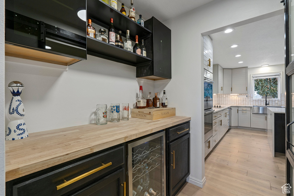 Bar featuring backsplash, wood counters, light wood-type flooring, and beverage cooler