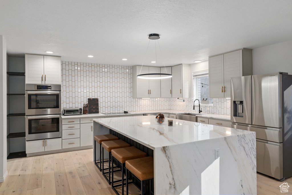 Kitchen with appliances with stainless steel finishes, a center island, backsplash, and light hardwood / wood-style flooring