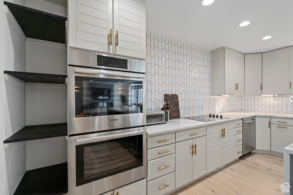Kitchen with appliances with stainless steel finishes, backsplash, white cabinetry, and light hardwood / wood-style flooring