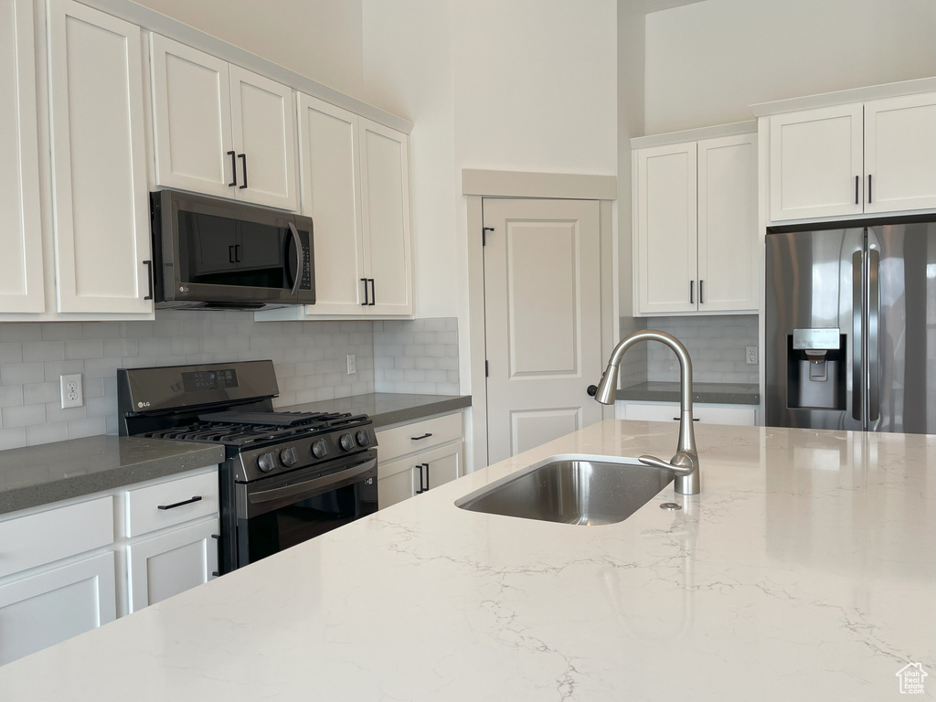 Kitchen featuring backsplash, sink, stainless steel appliances, and white cabinetry