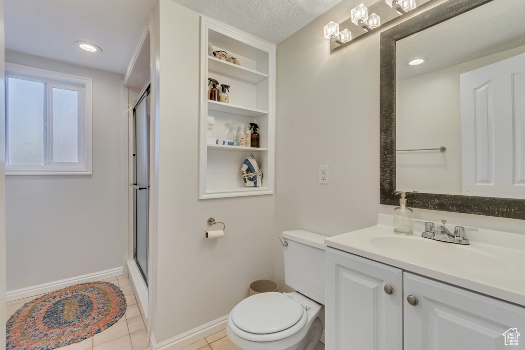 Bathroom featuring vanity with extensive cabinet space, a textured ceiling, walk in shower, toilet, and tile floors