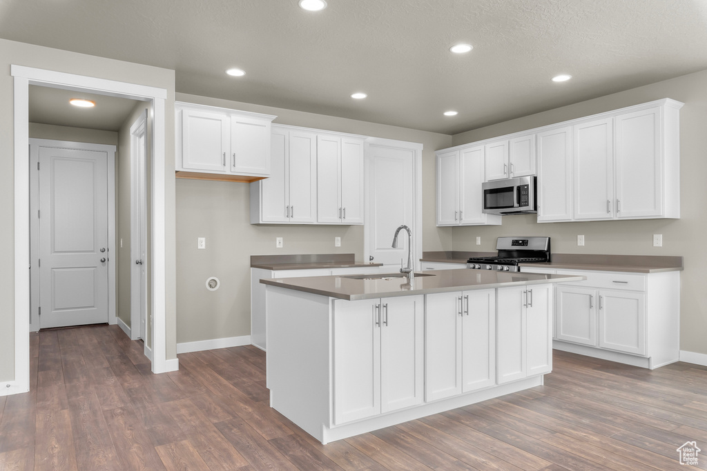 Kitchen with hardwood / wood-style floors, appliances with stainless steel finishes, white cabinetry, and a kitchen island with sink