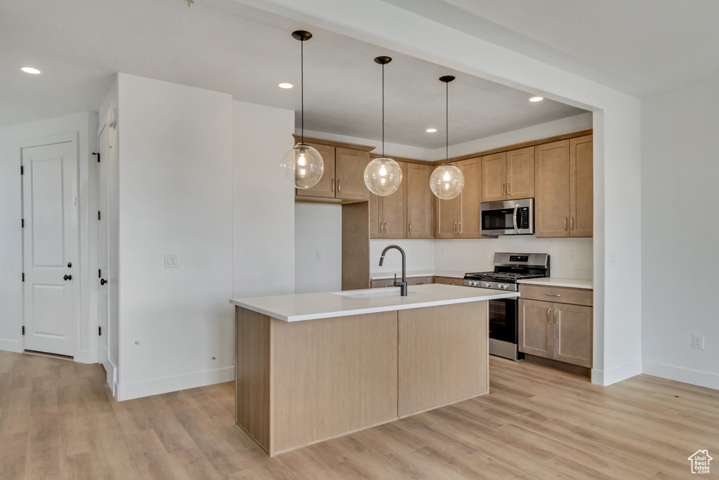 Kitchen with decorative light fixtures, appliances with stainless steel finishes, an island with sink, and light wood-type flooring