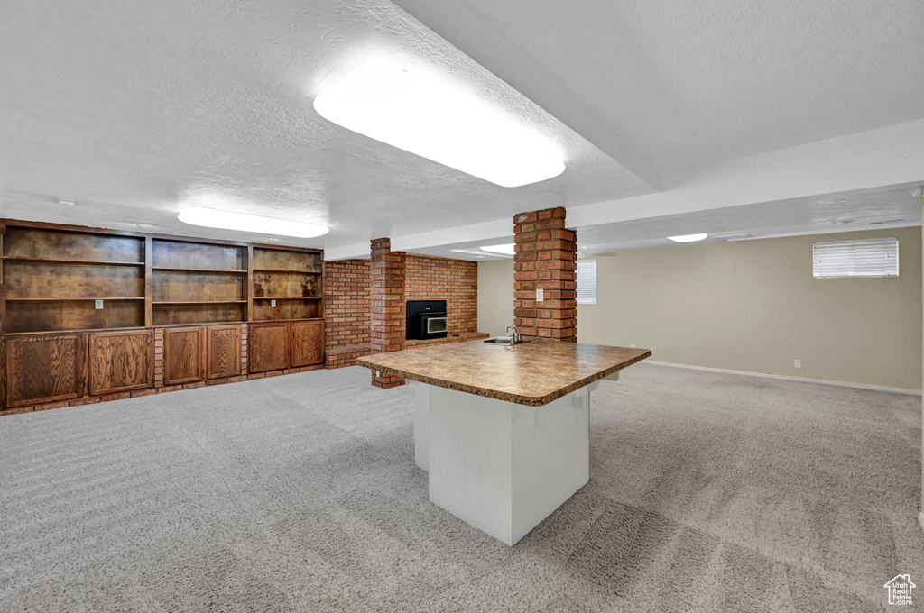 Basement featuring a fireplace, a textured ceiling, light carpet, sink, and a wood stove