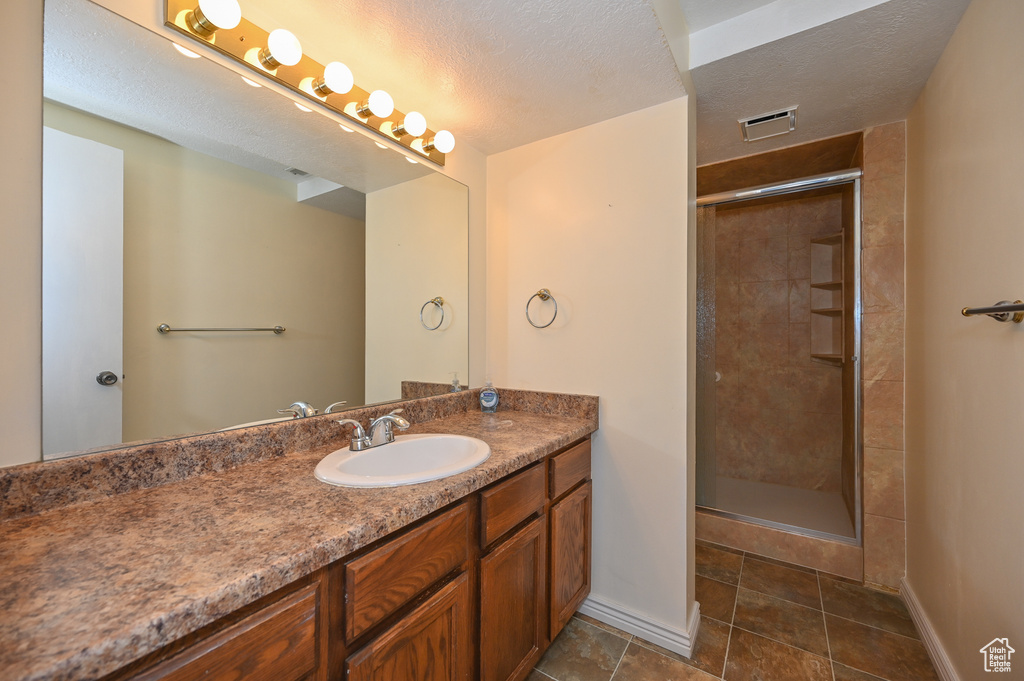 Bathroom with a shower with door, large vanity, tile floors, and a textured ceiling