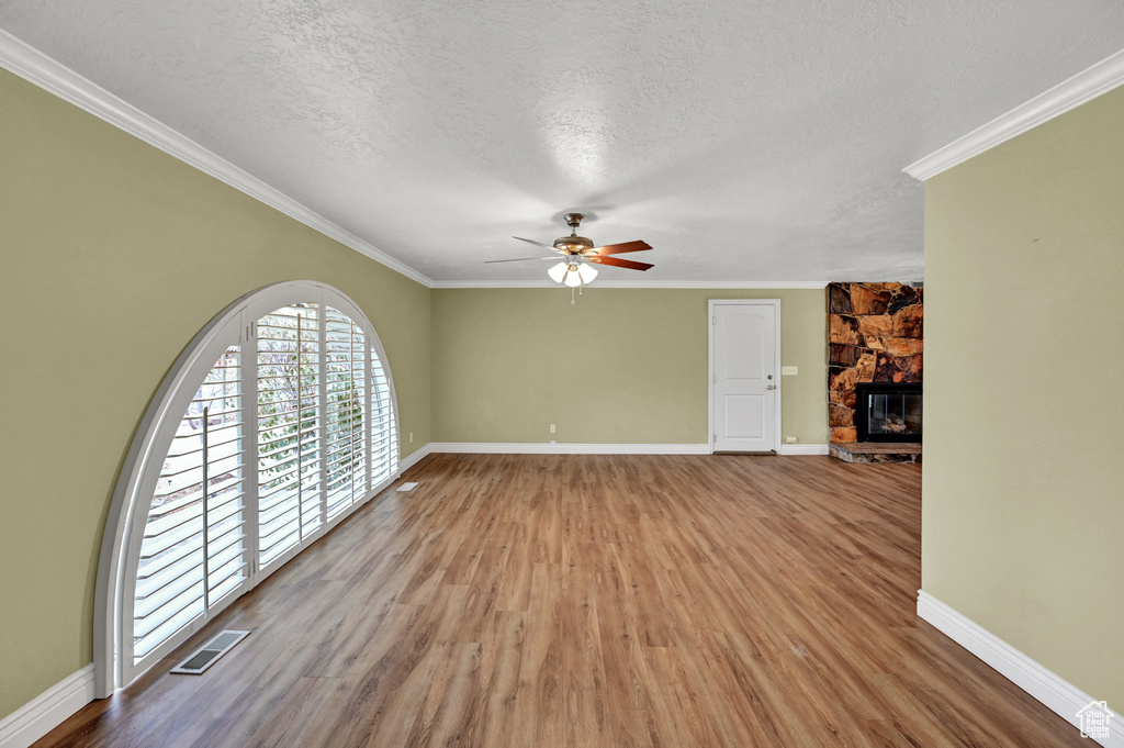 Empty room with ceiling fan, crown molding, a textured ceiling, a fireplace, and hardwood / wood-style floors