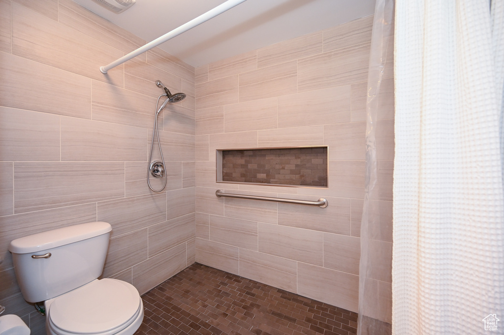 Bathroom featuring tile walls, toilet, and a shower with shower curtain