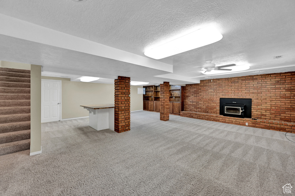 Basement with light carpet, a fireplace, brick wall, ceiling fan, and a textured ceiling