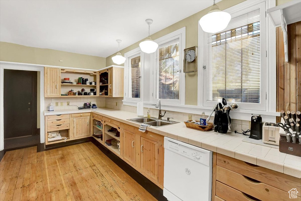 Kitchen with backsplash, light hardwood / wood-style floors, white dishwasher, and decorative light fixtures