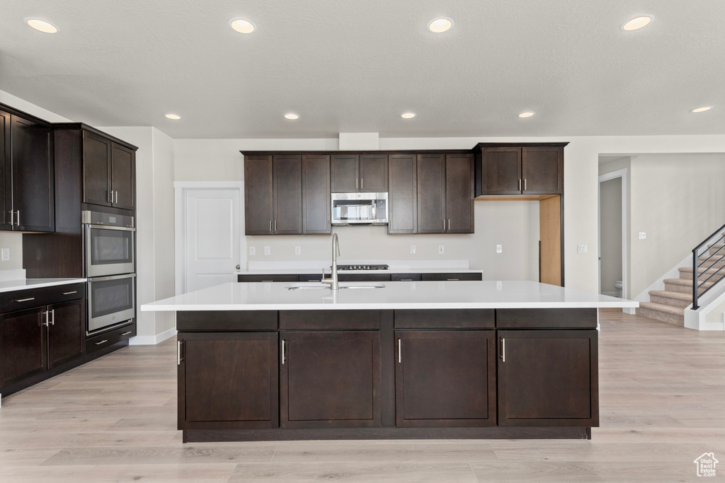 Kitchen featuring a kitchen island with sink, appliances with stainless steel finishes, light hardwood / wood-style flooring, and dark brown cabinetry