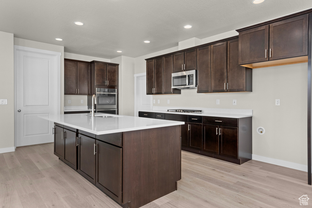 Kitchen featuring sink, appliances with stainless steel finishes, a center island with sink, light hardwood / wood-style floors, and dark brown cabinetry