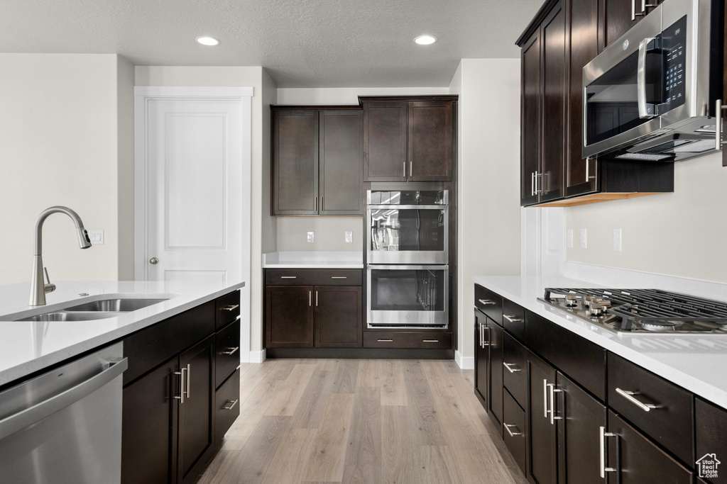Kitchen with dark brown cabinetry, sink, stainless steel appliances, and light hardwood / wood-style floors