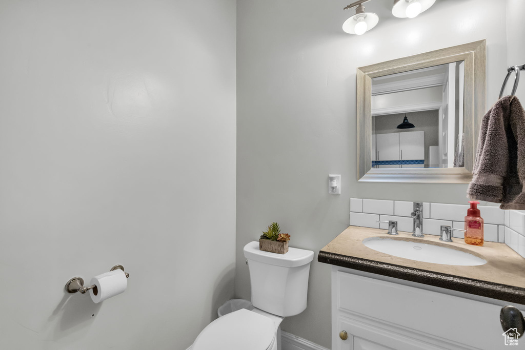 Bathroom with vanity with extensive cabinet space, tasteful backsplash, and toilet