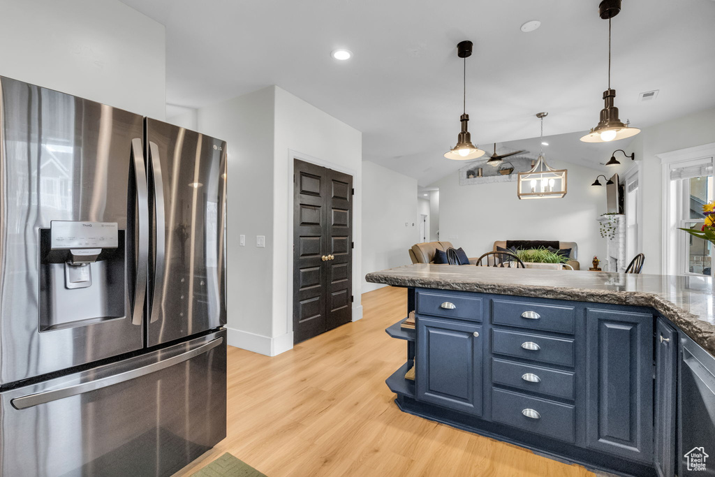 Kitchen featuring blue cabinets, stainless steel fridge with ice dispenser, light hardwood / wood-style flooring, dark stone countertops, and pendant lighting