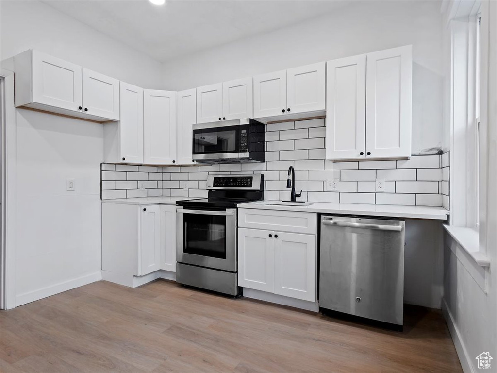 Kitchen with appliances with stainless steel finishes, light hardwood / wood-style floors, tasteful backsplash, white cabinetry, and sink
