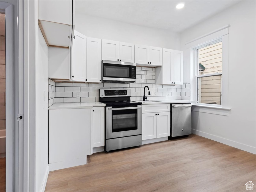 Kitchen featuring appliances with stainless steel finishes, light hardwood / wood-style flooring, backsplash, white cabinetry, and sink