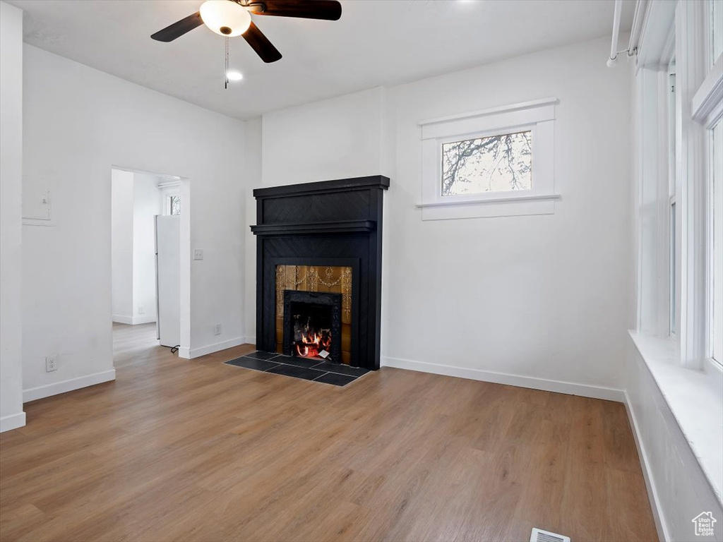 Unfurnished living room with a fireplace, ceiling fan, and light wood-type flooring