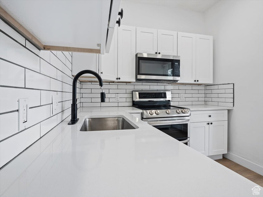 Kitchen featuring appliances with stainless steel finishes, wood-type flooring, white cabinets, and sink
