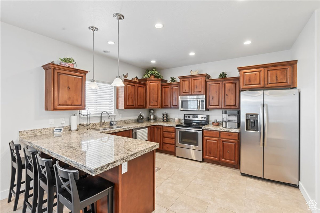 Kitchen with appliances with stainless steel finishes, light tile floors, sink, a breakfast bar area, and pendant lighting