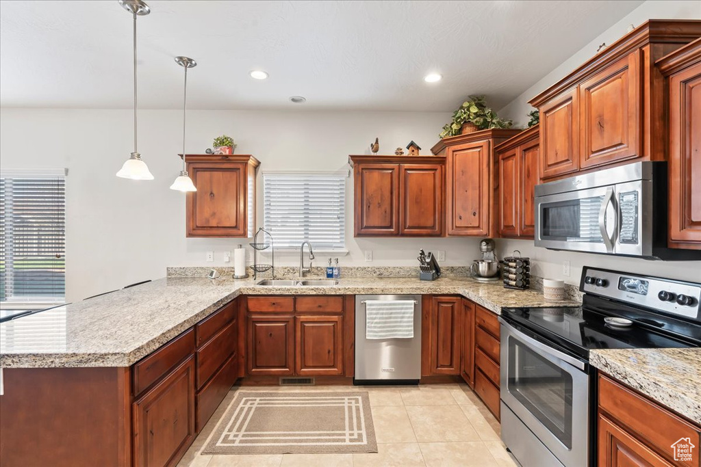 Kitchen with light stone countertops, appliances with stainless steel finishes, hanging light fixtures, sink, and light tile floors