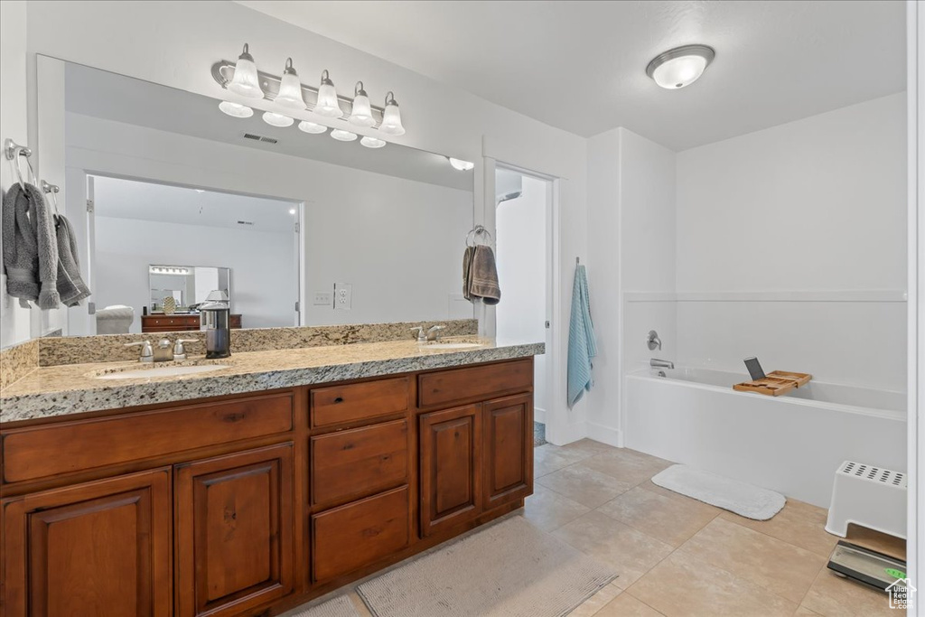 Bathroom featuring tile flooring, a bathtub, vanity with extensive cabinet space, and dual sinks