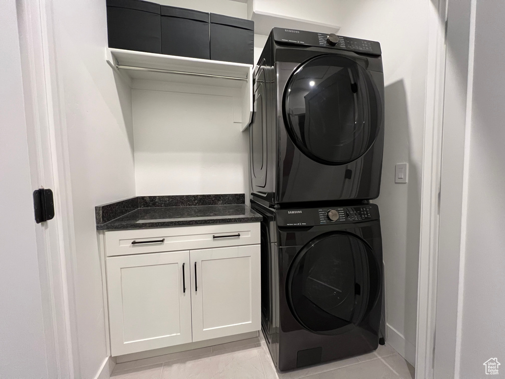Washroom with cabinets, stacked washer and dryer, and light tile flooring