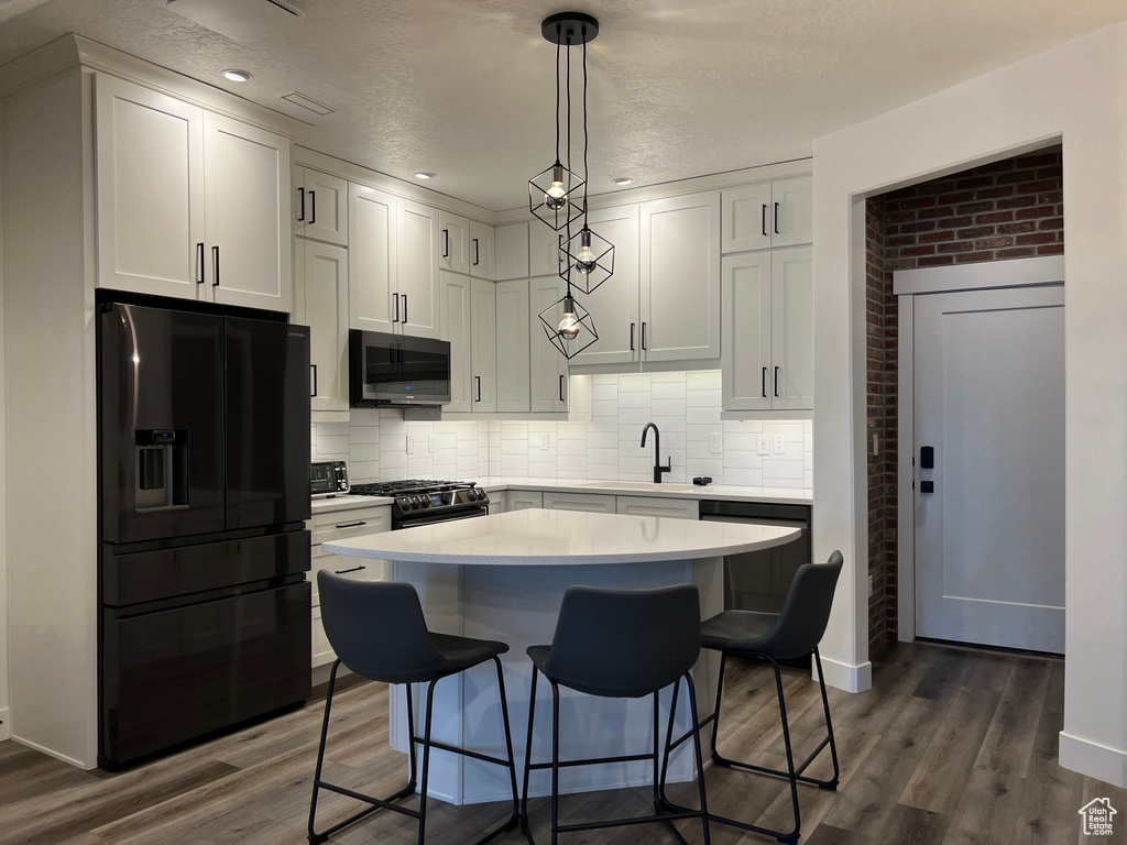 Kitchen featuring pendant lighting, dark wood-type flooring, white cabinetry, and black appliances