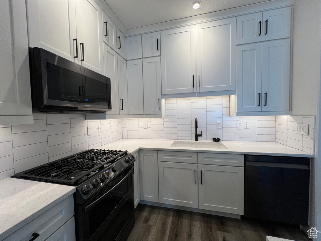 Kitchen with white cabinets, dark hardwood / wood-style flooring, black appliances, sink, and tasteful backsplash