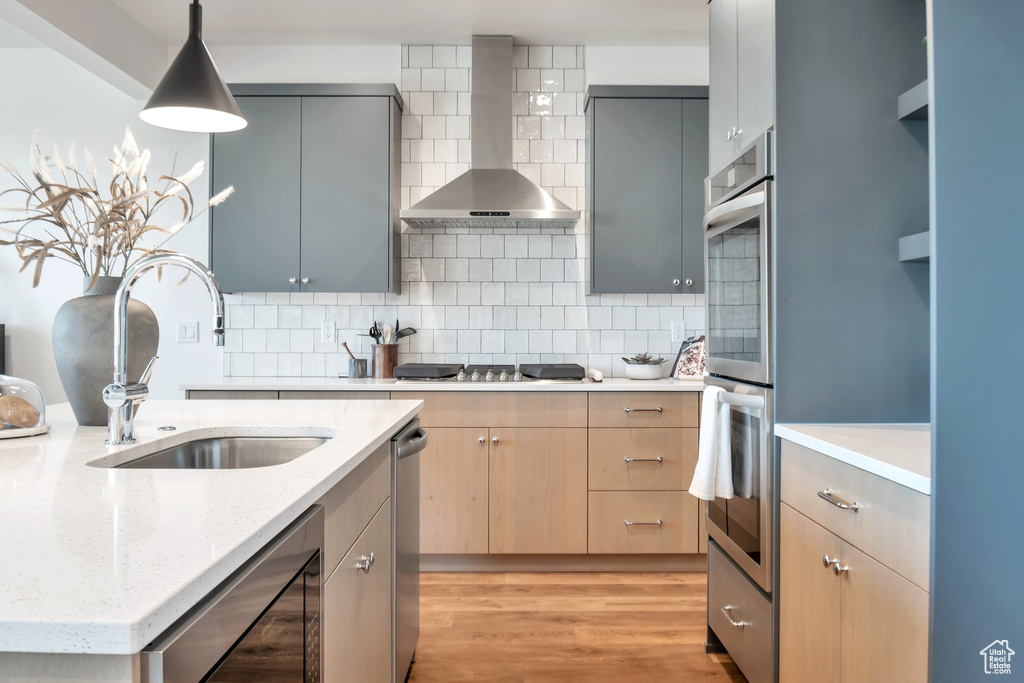Kitchen with decorative light fixtures, gray cabinets, light hardwood / wood-style flooring, tasteful backsplash, and wall chimney exhaust hood