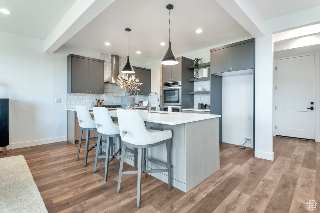 Kitchen featuring backsplash, gray cabinets, wall chimney range hood, and light wood-type flooring